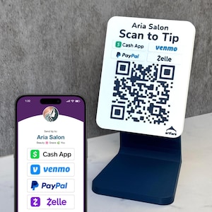 May include: Aria Salon tip stand with a QR code and payment options. The stand is navy blue, holding a white sign with "Scan to Tip" and payment logos for Cash App, Venmo, PayPal, and Zelle. A phone displays the salon's payment details.