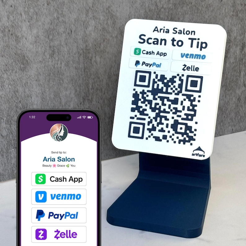 May include: Aria Salon tip stand with a QR code and payment options. The stand is navy blue, with a white top displaying "Scan to Tip" and payment logos for Cash App, Venmo, PayPal, and Zelle. A phone screen shows the salon's payment details.