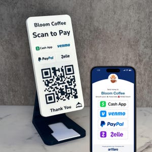May include: A white and black Bloom Coffee Scan to Pay stand with a QR code, Cash App, Venmo, PayPal, and Zelle logos. A smartphone displays a matching payment screen. The stand is on a gray surface.