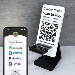 May include: A black and white payment stand with the text "Timber Crafts Scan to Pay" and QR codes for Cash App, Venmo, PayPal, and Zelle. A smartphone displays payment options. The stand is on a gray surface.