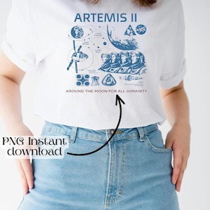 May include: White t-shirt with a blue graphic design featuring the text "ARTEMIS II" and illustrations of space-related elements. The phrase "AROUND THE MOON FOR ALL HUMANITY" is printed below the graphic. The shirt is paired with blue jeans.