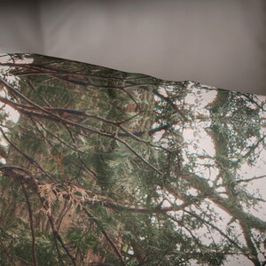 May include: A close-up of a fabric with a camouflage pattern featuring a forest scene with green trees and branches.