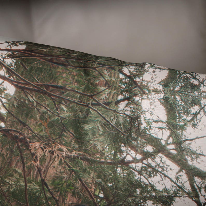 May include: A close-up of a fabric with a camouflage pattern featuring a forest scene with green trees and branches.