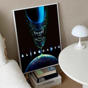 Puede incluir: Un póster enmarcado con una cabeza alienígena azul y verde goteando sobre una Tierra azul y verde. Las palabras "ALIEN EARTH" se muestran en blanco. El póster está en un marco blanco.