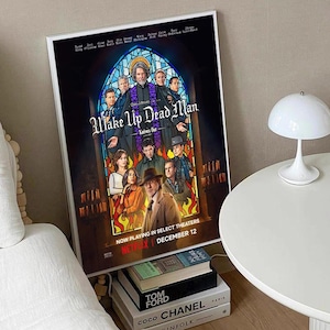 Peut inclure: Une affiche encadrée du film "Wake Up Dead Man: Knives Out", avec un design de vitrail représentant les personnages. L'affiche comprend le logo Netflix et le texte "Now Playing in Select Theaters December 12."