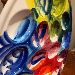 Pu&ograve; includere: Un piatto da portata in ceramica ovale e colorato con pi&ugrave; rientranze. Il piatto presenta un vivace design astratto con pennellate audaci nei toni del blu, giallo, verde, rosso e arancione. Il design &egrave; dipinto su uno sfondo bianco.