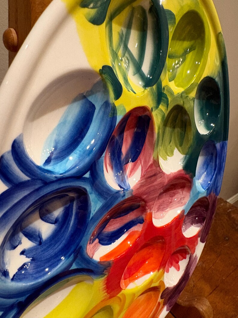 Pu&ograve; includere: Un piatto da portata in ceramica ovale e colorato con pi&ugrave; rientranze. Il piatto presenta un vivace design astratto con pennellate audaci nei toni del blu, giallo, verde, rosso e arancione. Il design &egrave; dipinto su uno sfondo bianco.