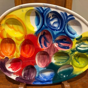 Pu&ograve; includere: Un vassoio da portata in ceramica ovale e colorato, con pi&ugrave; scomparti a forma di uovo. Il vassoio &egrave; dipinto con tonalit&agrave; vivaci di giallo, arancione, rosso, blu, verde e viola. Il design &egrave; artistico e accattivante, perfetto per servire antipasti.