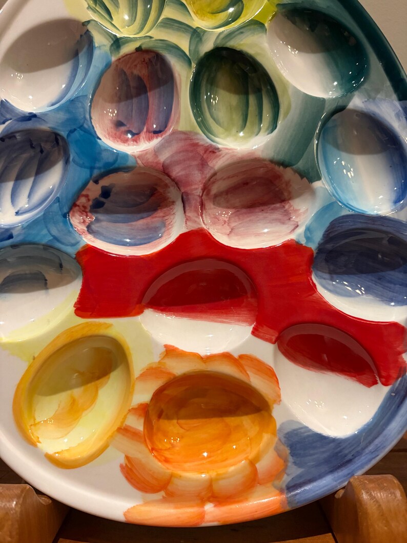 May include: A colorful, oval-shaped ceramic serving platter with multiple egg-shaped indentations. The platter features a vibrant palette of colors, including blue, red, yellow, and green, with a glossy finish. Ideal for serving deviled eggs or appetizers.
