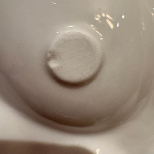 Pu&ograve; includere: Primo piano di un oggetto in ceramica bianca con un dettaglio circolare strutturato. L'oggetto ha una superficie liscia e lucida con sottili variazioni di tono. L'elemento circolare &egrave; leggermente rialzato e ha una consistenza ruvida.