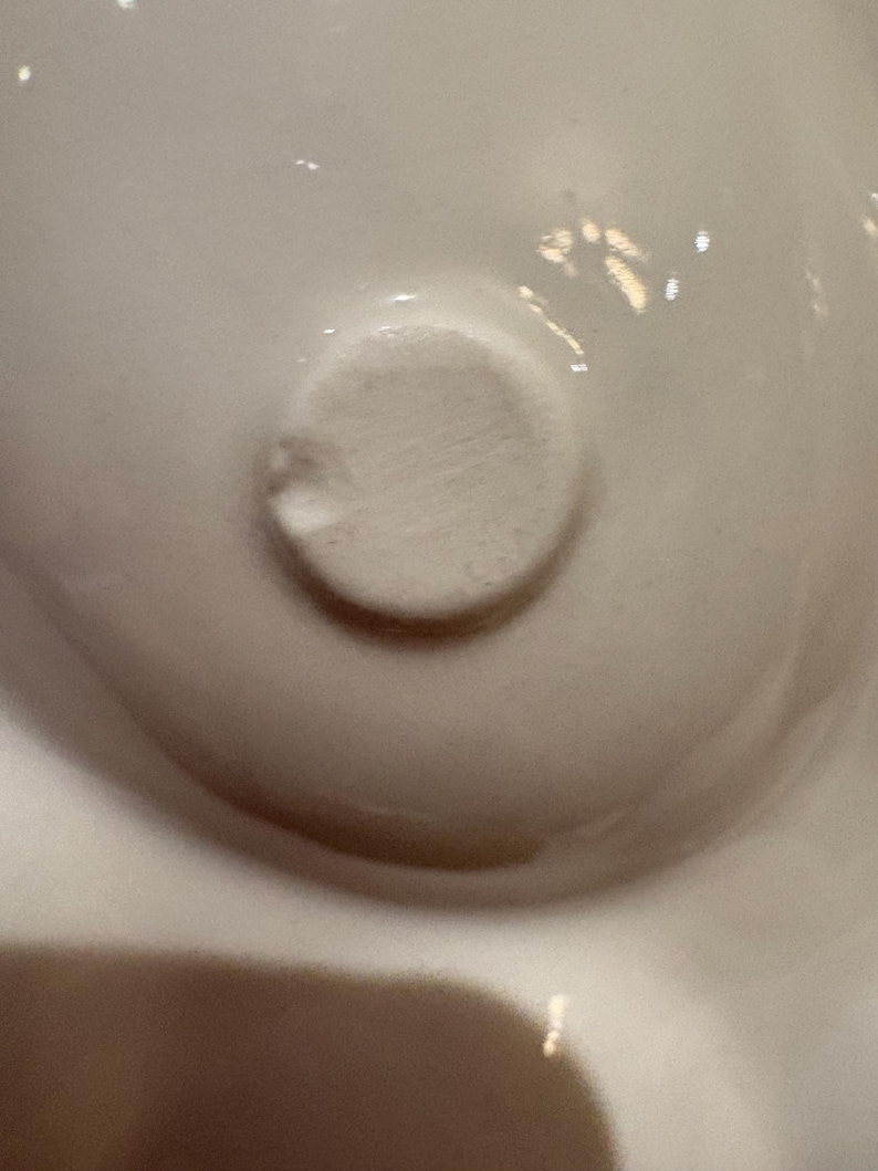 Pu&ograve; includere: Primo piano di un oggetto in ceramica bianca con un dettaglio circolare strutturato. L'oggetto ha una superficie liscia e lucida con sottili variazioni di tono. L'elemento circolare &egrave; leggermente rialzato e ha una consistenza ruvida.