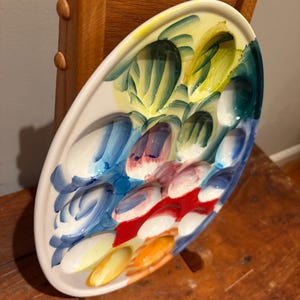 May include: Oval ceramic serving platter with a colorful abstract design. The platter features a white base with a painted pattern of blue, red, yellow, and green brushstrokes. The platter is displayed on a wooden surface.