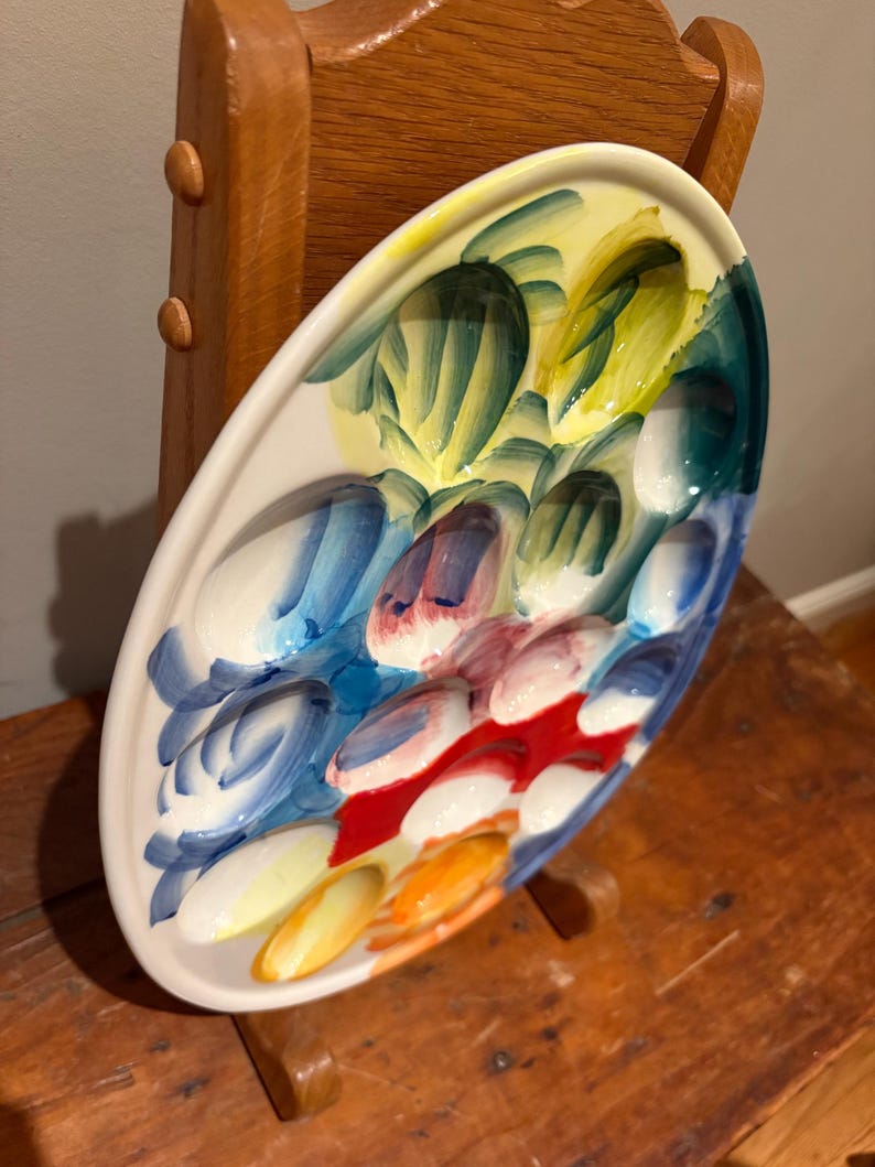 May include: Oval ceramic serving platter with a colorful abstract design. The platter features a white base with a painted pattern of blue, red, yellow, and green brushstrokes. The platter is displayed on a wooden surface.