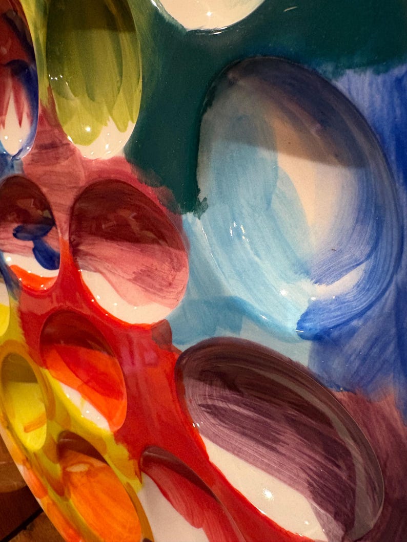 Pu&ograve; includere: Primo piano di un colorato piatto da portata in ceramica con finitura lucida. Il piatto presenta un design vibrante con varie forme e colori, tra cui rosso, giallo, blu, verde e viola. Il design include diverse rientranze ovali.