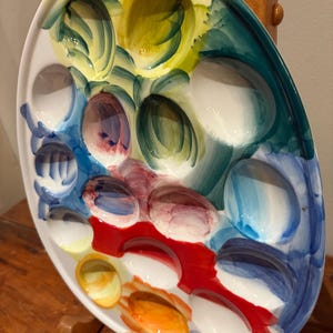 May include: Oval ceramic serving platter with multiple compartments, hand-painted with vibrant colors. The palette includes shades of yellow, blue, red, and white. The platter is designed for serving appetizers or small portions.
