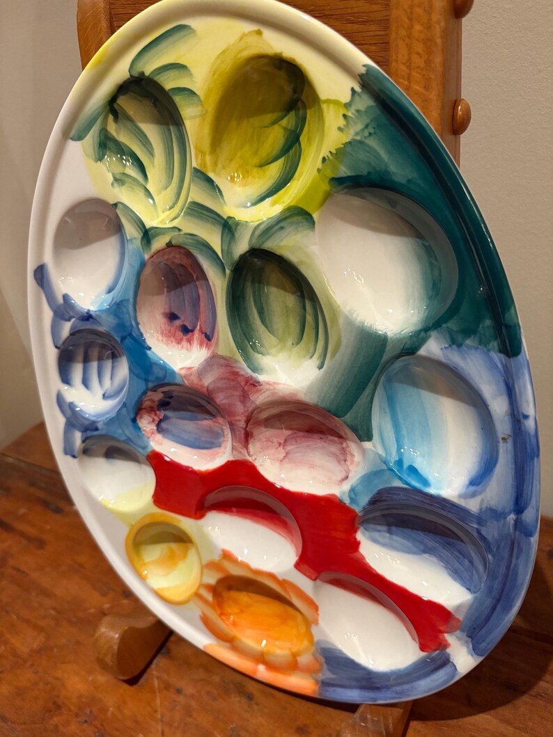 May include: Oval ceramic serving platter with multiple compartments, hand-painted with vibrant colors. The palette includes shades of yellow, blue, red, and white. The platter is designed for serving appetizers or small portions.