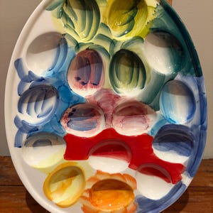 May include: Oval ceramic deviled egg serving platter with a colorful hand-painted design. The platter features egg-shaped indentations and is decorated with vibrant hues of yellow, blue, green, red, and orange.