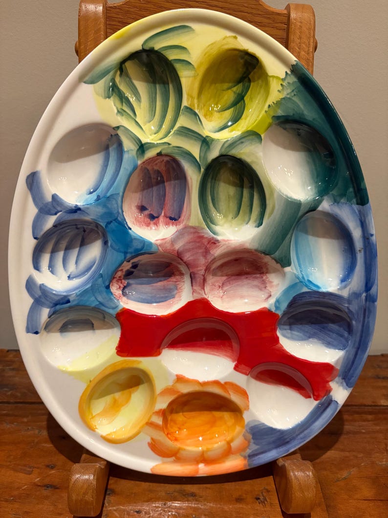 May include: Oval ceramic deviled egg serving platter with a colorful hand-painted design. The platter features egg-shaped indentations and is decorated with vibrant hues of yellow, blue, green, red, and orange.