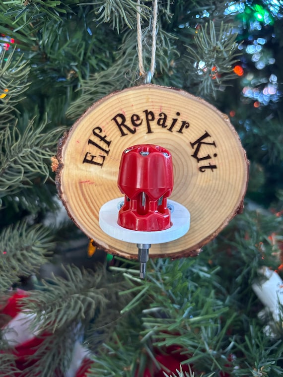 A handmade wooden Christmas ornament styled as an 'Elf Repair Kit' complete with a tiny screwdriver — a winking nod to the maker/DIY crowd that earns a second look on any tree.