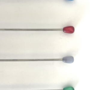 Könnte beinhalten: Vier Cocktail-Rührstäbchen aus Edelstahl mit tropfenförmigen, farbigen Spitzen. Die Spitzen sind blau, rot, lavendelfarben und grün. Die Rührstäbchen sind vertikal vor einem weißen Hintergrund angeordnet. Ideal zum Mixen von Getränken.