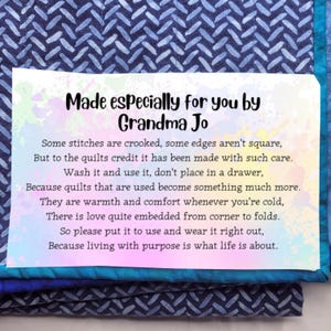 May include: A rectangular white card with a colorful watercolor splash background featuring the black text: Made especially for you by Grandma Jo, followed by a poem about quilts, placed on a dark blue fabric with a herringbone pattern.