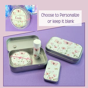 May include: A collection of personalized lip balm tins and containers. The tins are silver and feature a floral and butterfly design. One container is open, revealing a lip balm tube and a round container with the name "Emily".