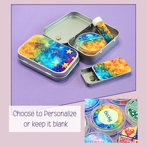 May include: Several small, rectangular and round metal tins with colorful galaxy designs. One tin is open, revealing a small round container and a tube. The text "Choose to Personalize or keep it blank" is visible.