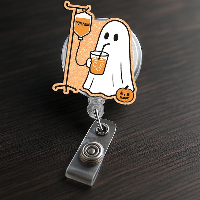 May include: A Halloween-themed badge reel showing a cartoon ghost drinking from a beverage with ice cubes. The ghost is next to a pumpkin and an IV bag labelled "PUMPKIN". The reel has a retractable cord and a metal clip.