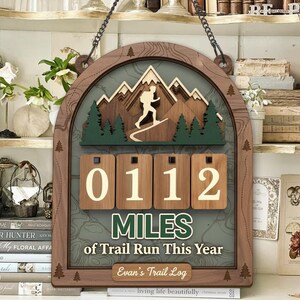 May include: Wooden trail run log with a mountain scene and the text "0112 MILES of Trail Run This Year." The log features a hiker silhouette, green trees, and a personalized nameplate. It is designed to be hung.