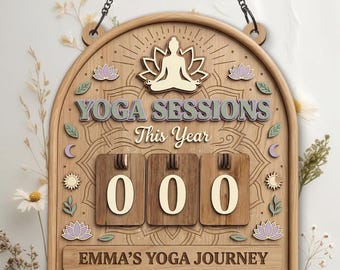 Op de afbeelding: Houten yogasessies-tellerbord met de tekst "YOGA SESSIONS This Year" en "EMMA'S YOGA JOURNEY". Het bord toont een lotusbloem, zon, maan en een mediterende figuur. De teller toont "000".