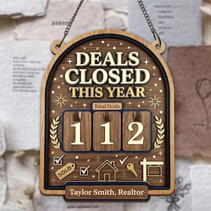 Könnte beinhalten: Holzschild mit dem Text "DEALS CLOSED THIS YEAR" und der Zahl "112". Das Schild hat einen dunkelblauen und goldenen Rand, mit dem Namen "Taylor Smith, Realtor" unten. Enthält Symbole für verkauft, Häkchen, ein Haus, einen Schlüssel und ein Verkaufsschild.