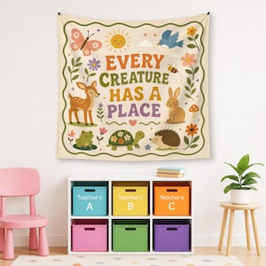 May include: A square wall tapestry with a cream background and a wavy green border. The text reads EVERY CREATURE HAS A PLACE in orange, green, and purple. Illustrations include a butterfly, sun, bird, deer, bee, rabbit, frog, turtle, and hedgehog.
