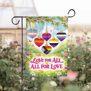 May include: A garden flag with a floral design and the text "Love for All, All for Love." The flag features heart-shaped ornaments with LGBTQ+ pride flag designs, hanging from a flowering branch against a blue sky.
