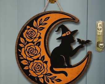 May include: A crescent moon-shaped wooden wall hanging featuring a black cat wearing a witch hat and holding a small bat. The design includes orange and black colors with a floral pattern of three roses along the left side of the moon.