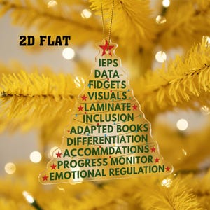 May include: Clear acrylic Christmas tree ornament with the words "IEPS DATA FIDGETS VISUALS LAMINATE INCLUSION ADAPTED BOOKS DIFFERENTIATION ACCOMMODATIONS PROGRESS MONITOR EMOTIONAL REGULATION" in green text. The ornament is hanging on a yellow Christmas tree.