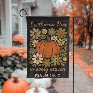 Könnte beinhalten: Schwarze Gartenflagge mit Kürbis- und Blumendesign. Die Flagge trägt den Text "I will praise Him in every season" und "PSALM 146:2". Der Kürbis ist orange, umgeben von grünen, gelben und cremefarbenen Blumen.