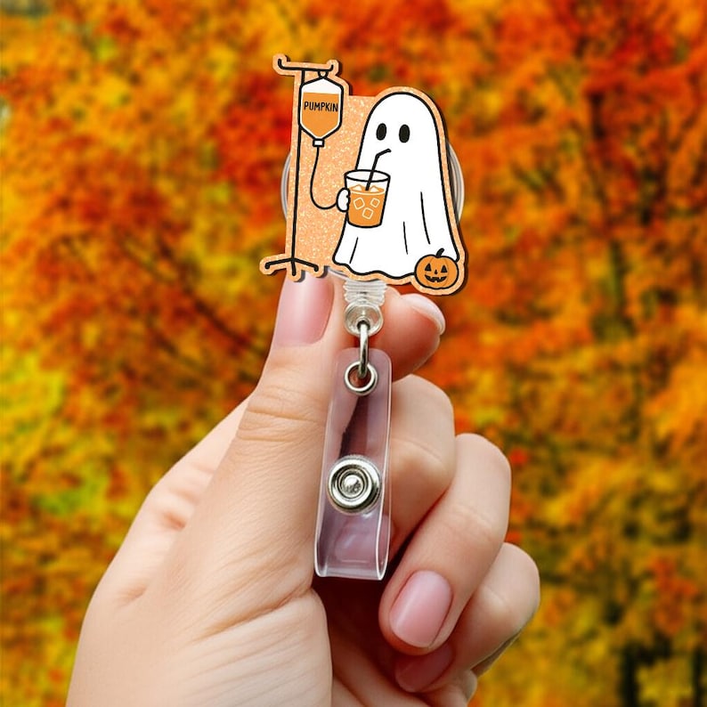 May include: A Halloween-themed badge reel with a cartoon ghost drinking from a cup, and a pumpkin IV drip. The badge reel has a clear plastic clip and a retractable cord. The word "PUMPKIN" is on the IV bag.