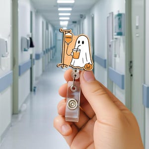 May include: A Halloween-themed badge reel with a cartoon ghost drinking from a cup, a pumpkin, and an IV bag. The badge reel is made of wood and has a clear plastic retractable holder.