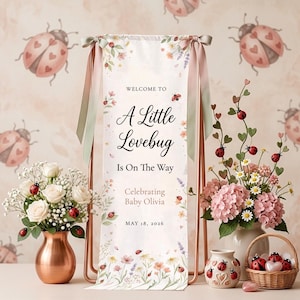 May include: A baby shower banner with the text "A Little Lovebug Is On The Way" and "Celebrating Baby Olivia, May 18, 2026." The banner is decorated with floral and ladybug accents. The scene includes floral arrangements and decorative items.