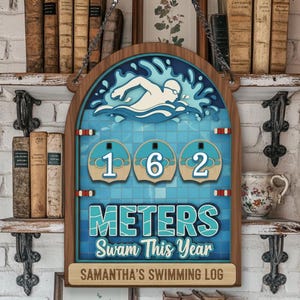 May include: Wooden swimming log sign with a swimmer graphic and the text "162 Meters Swam This Year". The sign is in shades of blue and brown, with a personalized name at the bottom. It hangs from a chain.