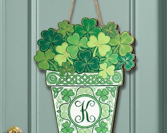 May include: Wooden door hanger with a green shamrock design in a pot. The pot is white and green with a Celtic knot design and the letter "K". The shamrocks are various shades of green, and the hanger is suspended by a natural rope.