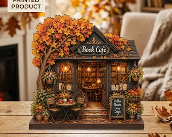 May include: A 2D flat printed product depicting a miniature book cafe with a large autumn tree, hanging flower baskets, and outdoor seating. The sign reads Book Cafe, and a chalkboard sign displays Coffee, Books, Cozy, Days. The scene features warm lighting.