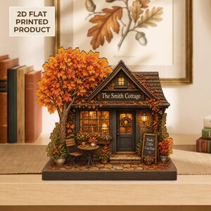 Peut inclure: Un produit imprimé plat en 2D représentant un cottage miniature nommé The Smith Cottage, avec un grand arbre d'automne orange, une petite table avec des chaises et un panneau indiquant Books Coffee Cozy Days, sur une base en bois sombre.