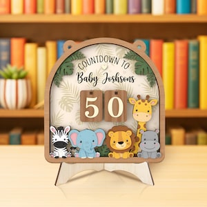 May include: Wooden countdown calendar with the text "COUNTDOWN TO Baby Joshsons" and the number "50". The calendar features a zebra, elephant, lion, giraffe, and hippo. The background has a leaf pattern.
