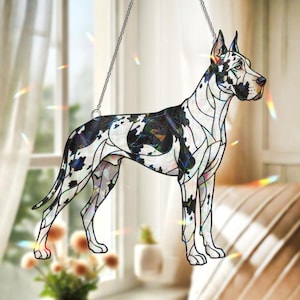 Op de afbeelding: Een gebrandschilderd glas Great Dane honden zonnevanger. De hond wordt afgebeeld in een staande pose met een zwart-witte gevlekte vacht, zwarte oren en een zwarte neus. De zonnevanger hangt aan een zilveren ketting.