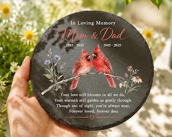 Può includere: Una targa commemorativa rotonda in ardesia nera con il testo In Loving Memory Mom & Dad 1945-2025 1945-2025, due cardinali rossi appollaiati su un ramo, illustrazioni floreali e la poesia Your love still blooms in all we do, Your warmth still guides us gently through, Though out of sight, you're always near, Forever loved, forever dear.