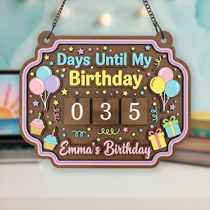 May include: Wooden birthday countdown sign with the text "Days Until My Birthday" and "Emma's Birthday." The sign features balloons, cupcakes, and gifts. The countdown shows "035" days remaining. It hangs from a chain.