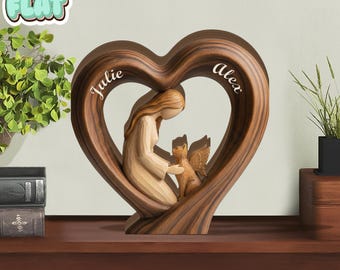 Può includere: Scultura in legno a forma di cuore raffigurante una donna e una creatura alata. I nomi "Julie" e "Alex" sono incisi sul cuore. La scultura è in legno scuro e poggia su una superficie di legno.