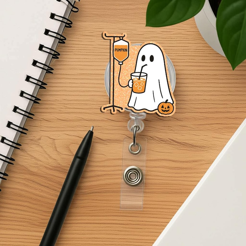 May include: A Halloween-themed badge reel with a cartoon ghost drinking from a cup, a pumpkin, and an IV drip. The IV bag reads "PUMPKIN". The reel has a clear plastic strap and a metal clip.