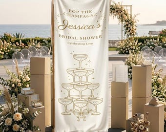 Può includere: Un banner color crema con testo dorato che recita "Pop the Champagne Jessica's Bridal Shower Celebrating Love". Un disegno a piramide di calici di champagne è sotto il testo. Lo striscione è esposto all'aperto con composizioni floreali e il mare sullo sfondo.